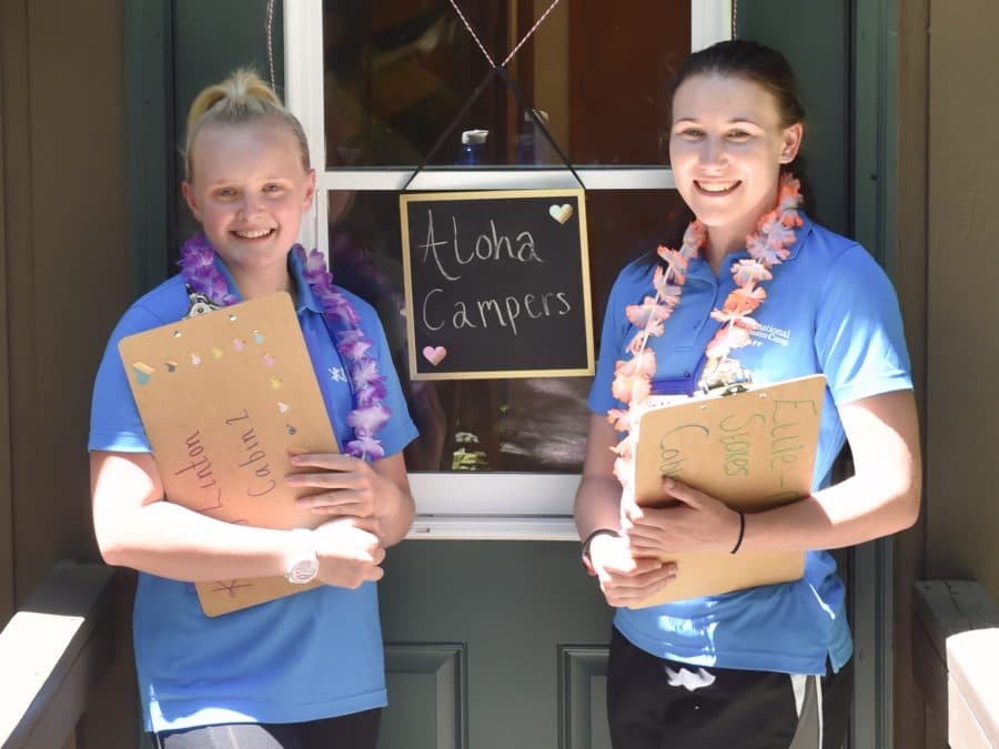Two female staff members holding clip boards and wearing leis